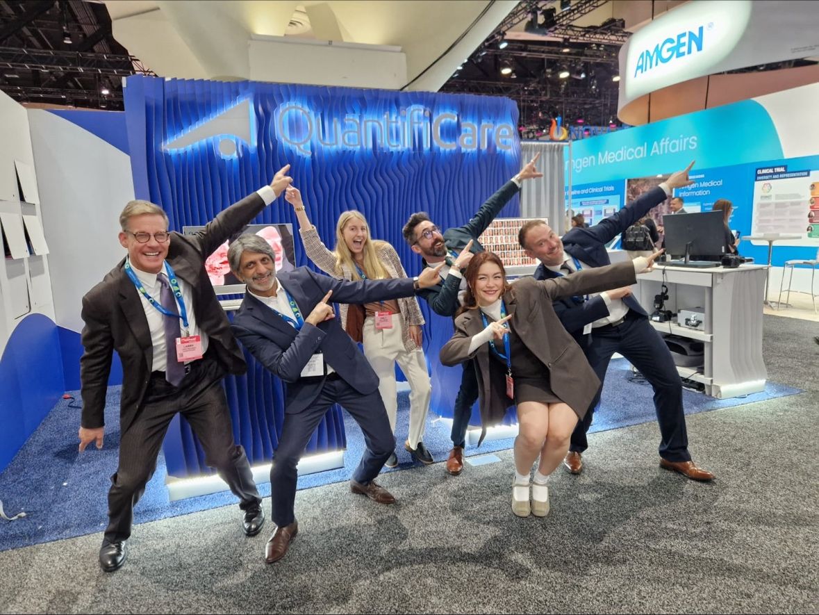 Quantificare team posing in front of the booth