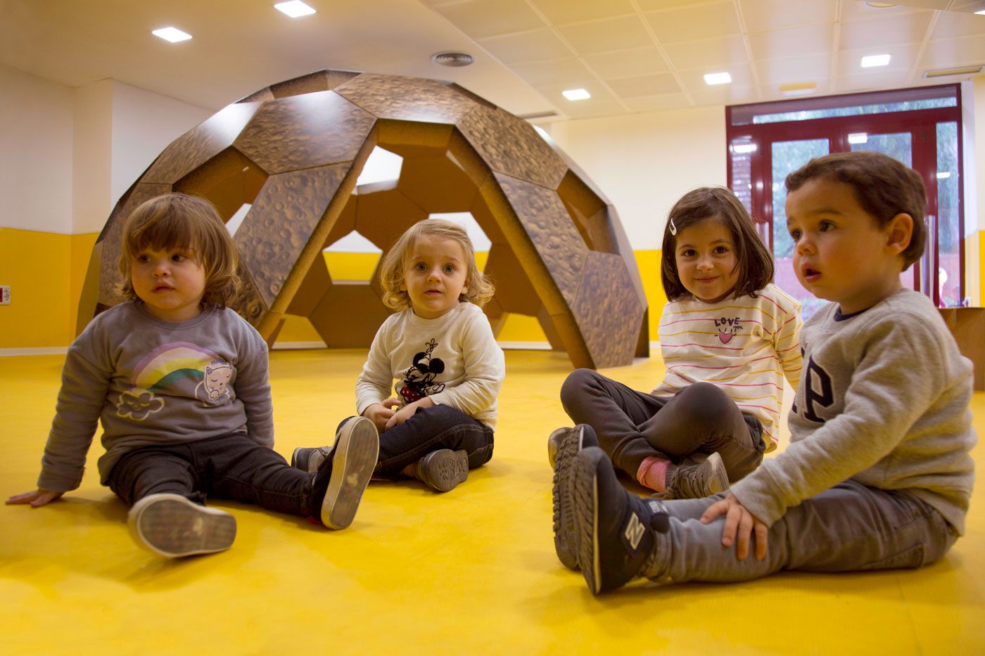 Niños sentados frente cúpula geodésica de cartón